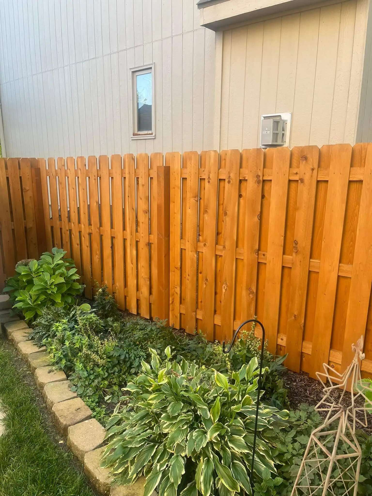 A recently stained fence in a yard with many plants.